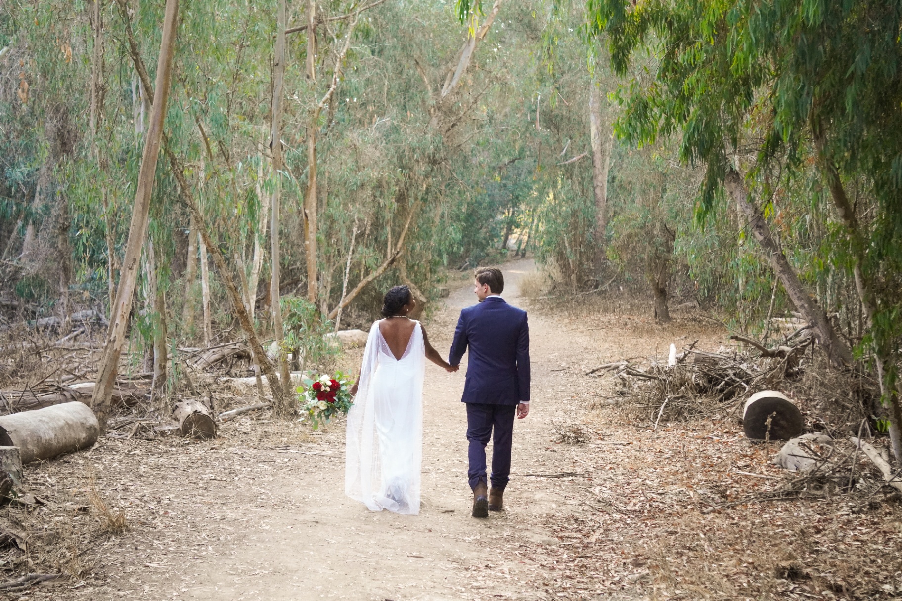 Bride and groom holding hands on a eucalyptus trail at Ellwood Bluffs near Santa Barbara