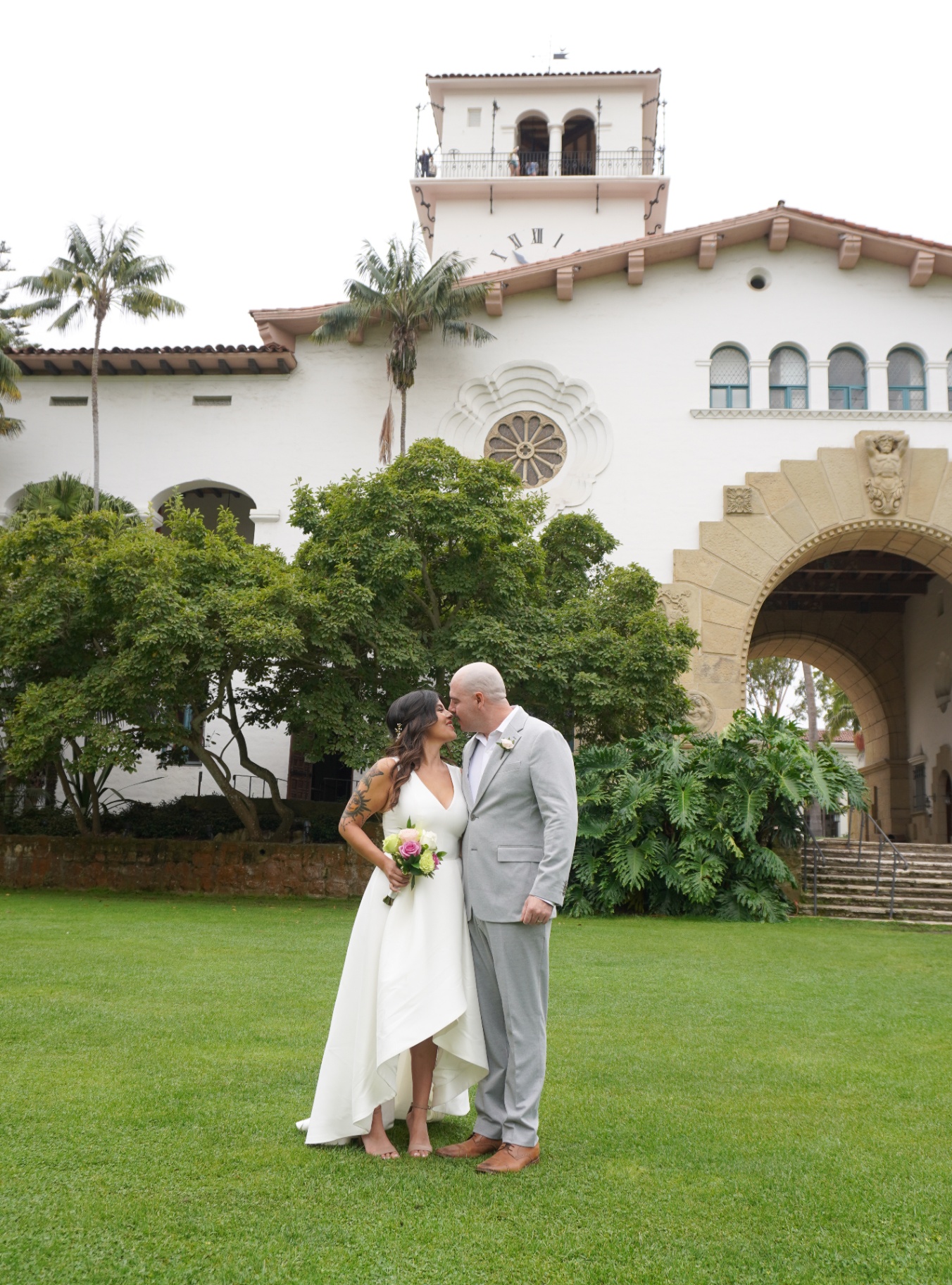 Bride and groom kissing on the Sunken Gardens lawn beneath the Santa Barbara Courthouse clock tower