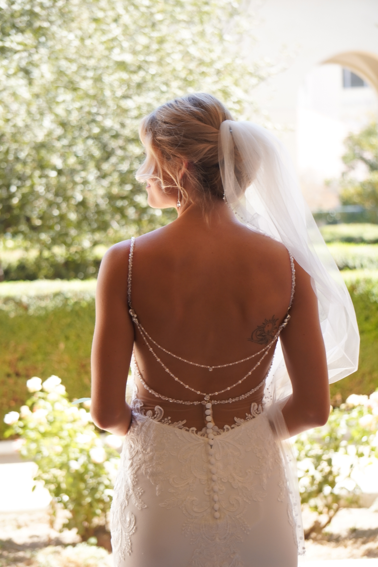 Bride in a beaded open-back lace wedding gown with cathedral veil in a Pasadena garden courtyard