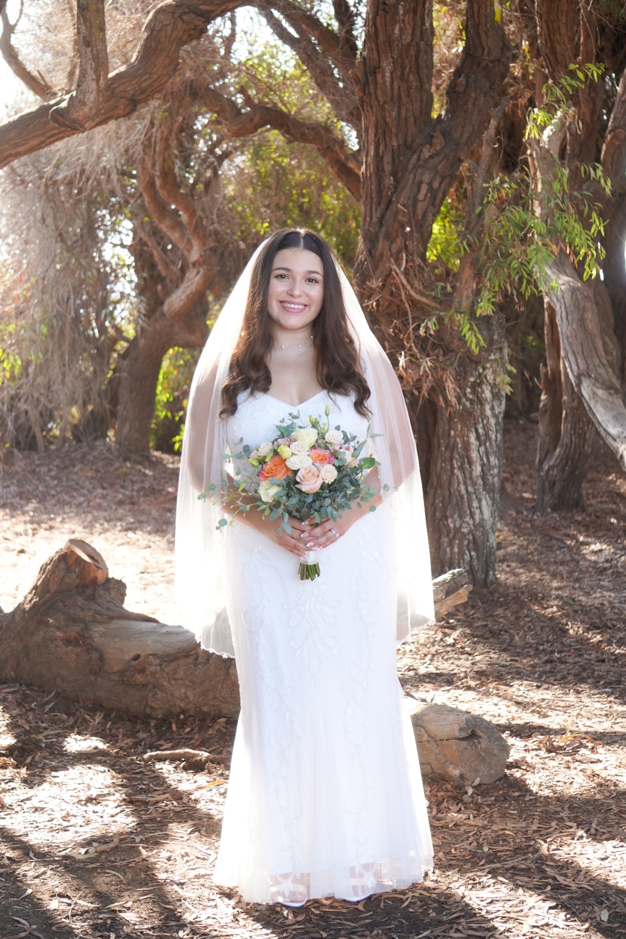 Smiling Santa Barbara bride with veil and bouquet beneath golden oak trees at Ellwood Bluffs