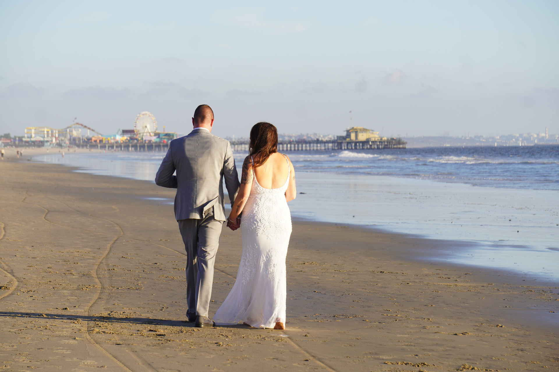 Santa Monica beach wedding couple walking hand-in-hand toward the Santa Monica Pier at golden hour